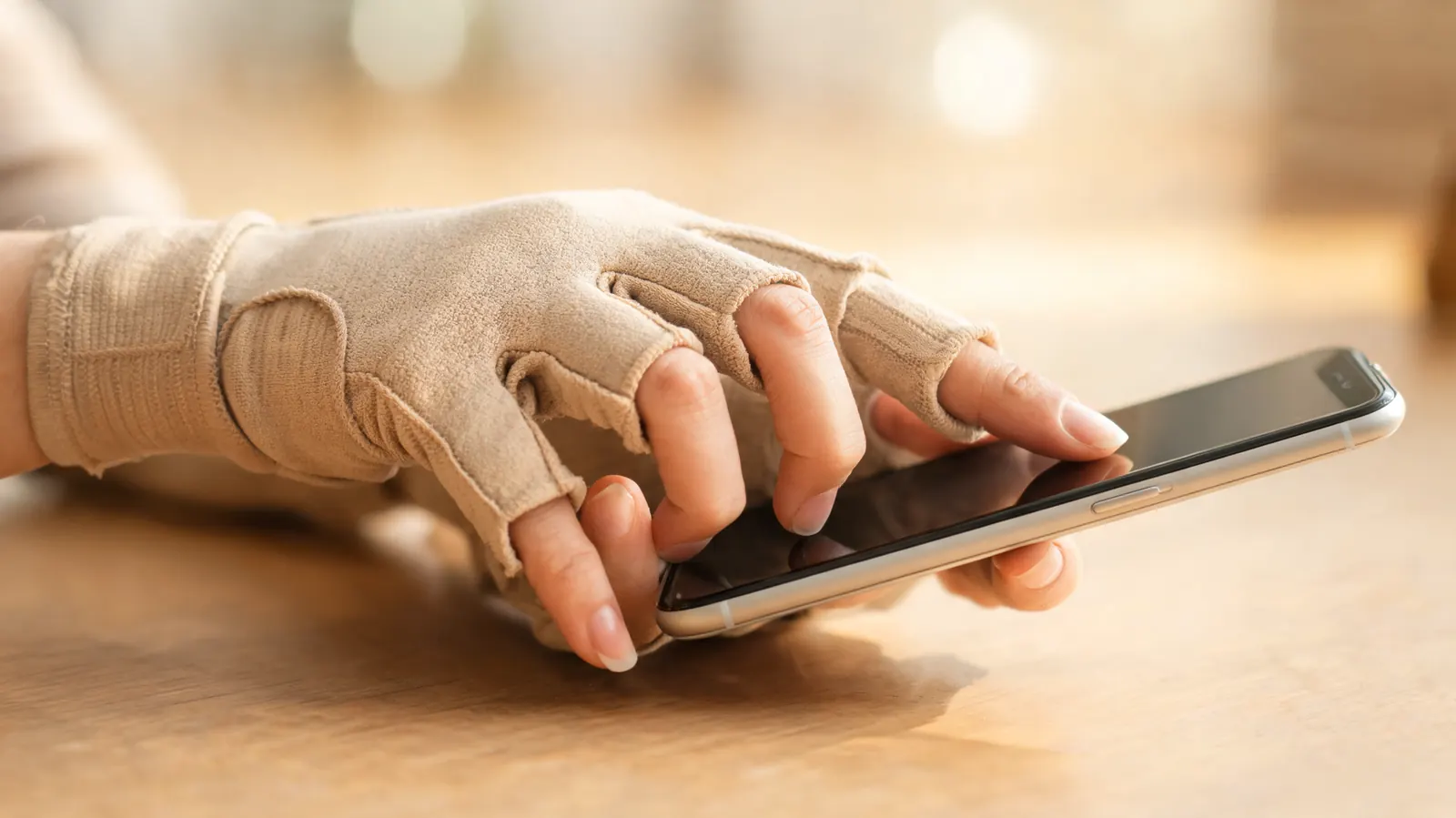 Close-up of one hand wearing a beige open-finger compression glove picking up a smartphone