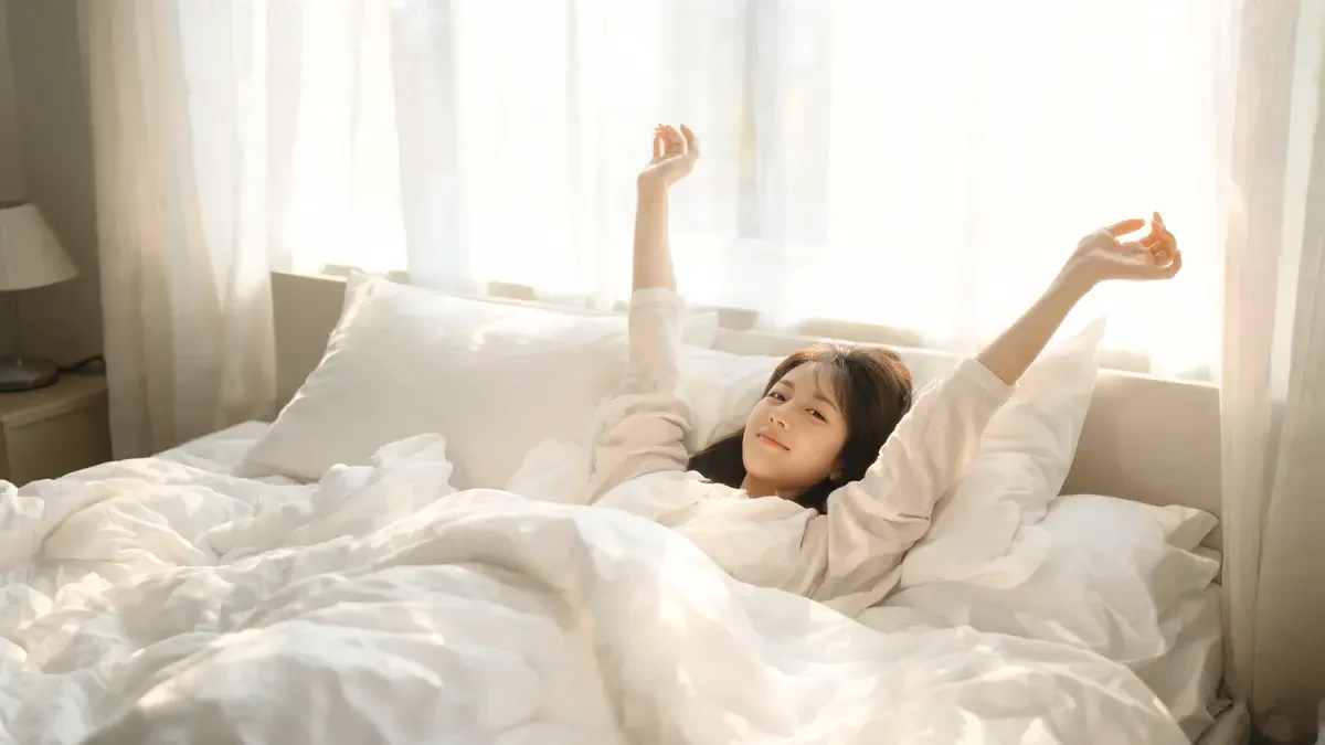 Person waking peacefully with a stretch in warm white bedding morning light