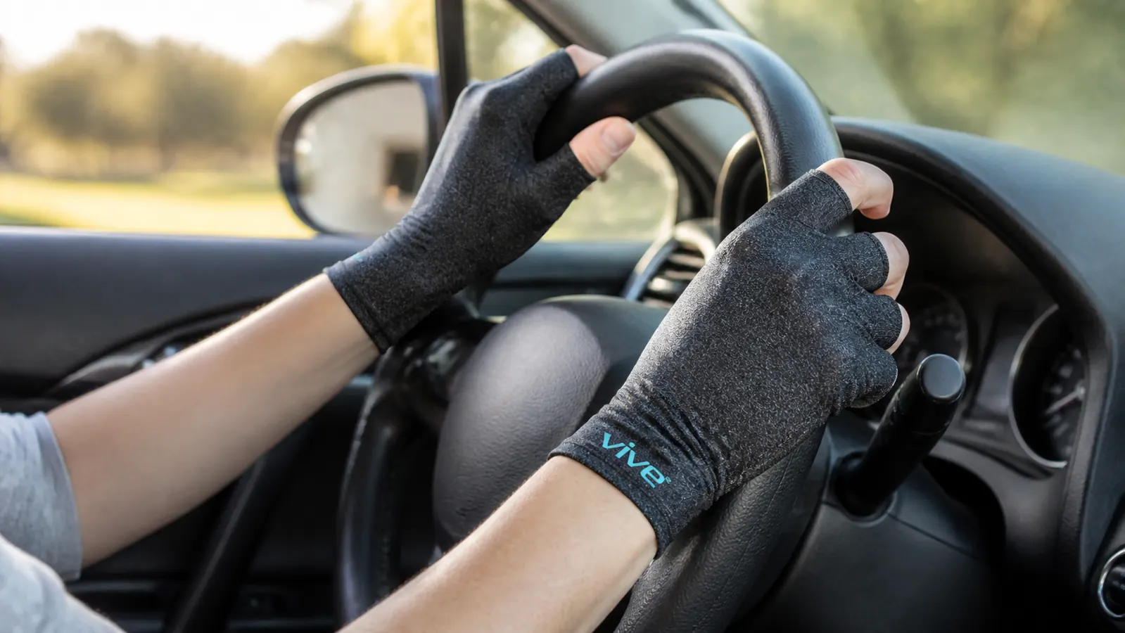 Close-up of hands wearing Vive open-finger compression arthritis gloves gripping a car steering wheel